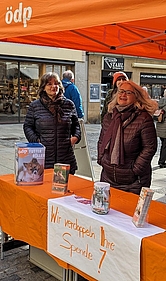 Bild 1: Infostand der ÖDP vom 30. Dezember 2023 für die Aktion "Futter statt Böller". Auf dem Plakat steht geschrieben "Wir verdoppeln ihre Spende". Von links: Anne Schlittmaier und Angela Büchner, dahinter verdeckt Dagmar Murmann-Patzek